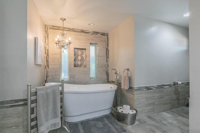 bathroom featuring tile walls, a chandelier, a freestanding tub, wainscoting, and a towel warmer