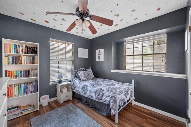 bedroom with wood finished floors, baseboards, multiple windows, and ceiling fan