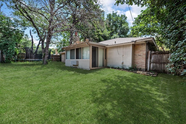 rear view of property featuring a trampoline, brick siding, a sunroom, and a chimney