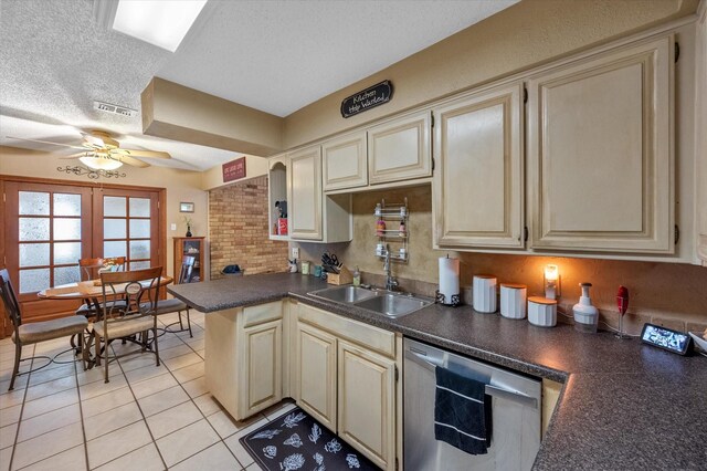 kitchen featuring stainless steel dishwasher, a sink, a ceiling fan, dark countertops, and cream cabinetry