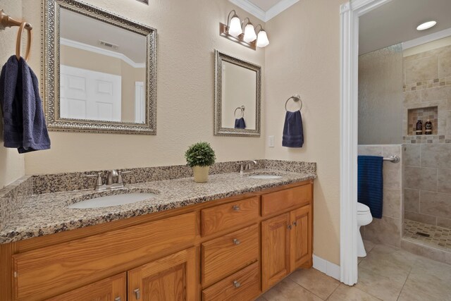 bathroom with ornamental molding, tile patterned flooring, toilet, tiled shower, and double vanity