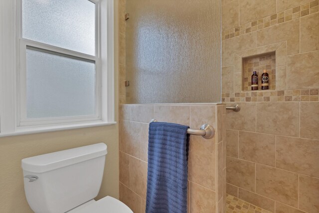 full bath featuring tiled shower and toilet