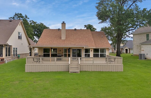 rear view of property with central AC unit, a lawn, a chimney, a deck, and roof with shingles