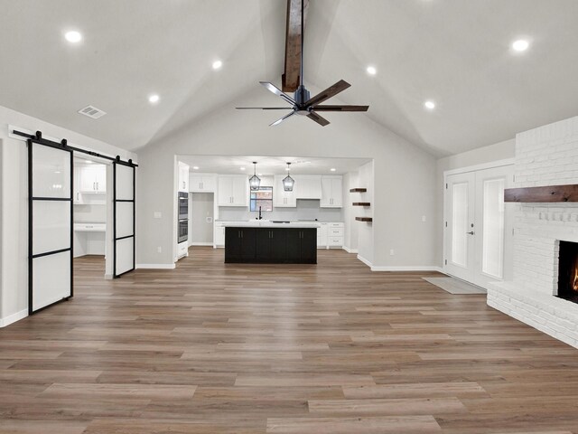 309 Rash Ln, Terrell, TX 75160 - unfurnished living room featuring a brick fireplace, a barn door, beamed ceiling, a ceiling fan, and light wood finished floors