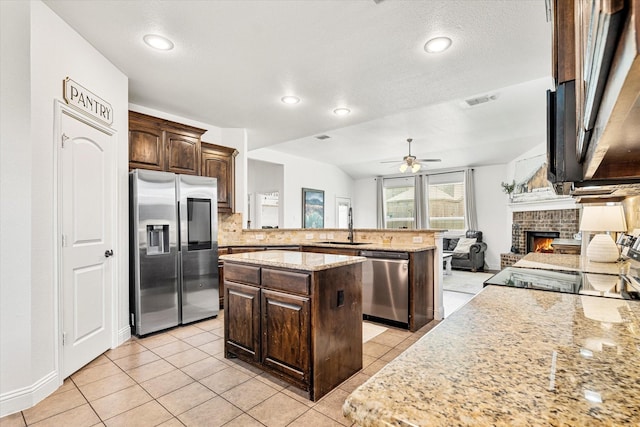 6273 El Capitan St, Fort Worth, TX 76179 - kitchen with stainless steel appliances, a peninsula, dark brown cabinets, ceiling fan, and a brick fireplace