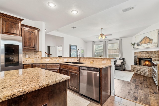 6273 El Capitan St, Fort Worth, TX 76179 - kitchen featuring stainless steel appliances, a brick fireplace, a sink, light stone counters, and vaulted ceiling