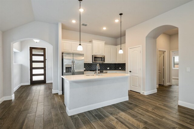 9117 Amistad Ln, Denton, TX 76226 - kitchen featuring appliances with stainless steel finishes, arched walkways, dark wood finished floors, light countertops, and decorative backsplash