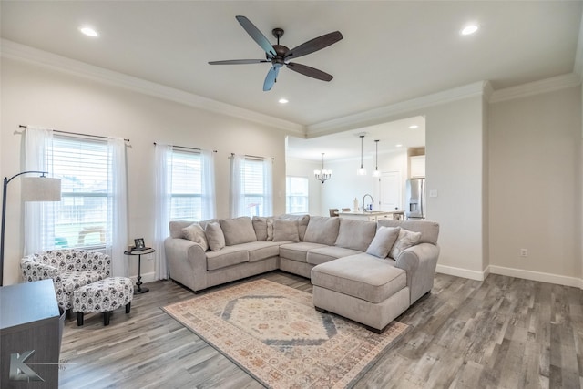 living room featuring ornamental molding, light wood-type flooring, ceiling fan, baseboards, and a chandelier