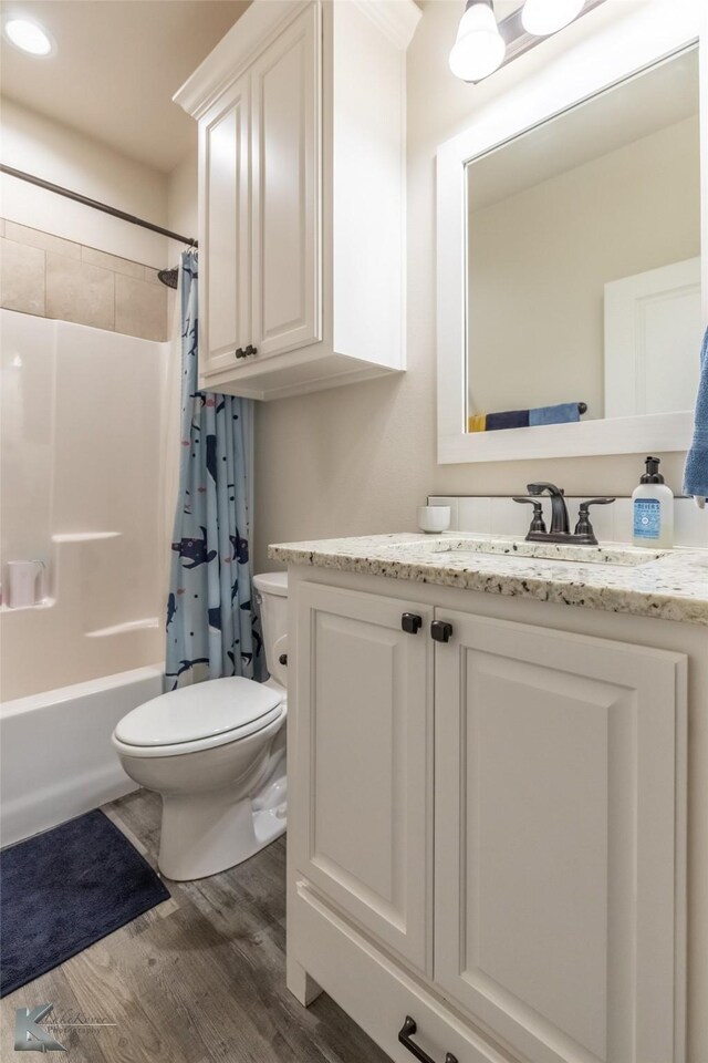full bath featuring toilet, wood finished floors, vanity, and shower / tub combo with curtain
