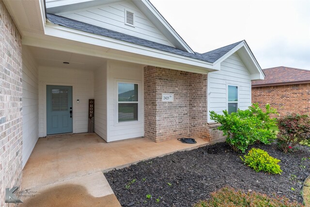 view of exterior entry with brick siding and roof with shingles