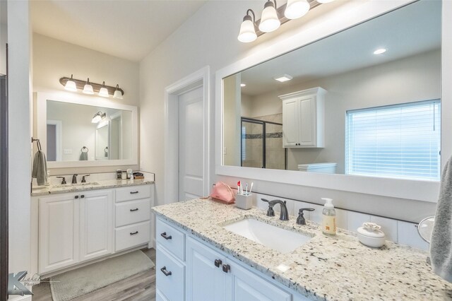 bathroom featuring a shower stall, two vanities, and wood finished floors