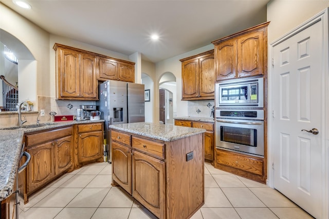 314 Trakehner Trl, Celina, TX 75009 - kitchen with stainless steel appliances, arched walkways, a sink, a center island, and brown cabinetry