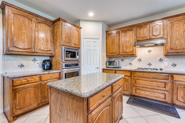 314 Trakehner Trl, Celina, TX 75009 - kitchen with stainless steel appliances, under cabinet range hood, light tile patterned floors, brown cabinets, and a center island