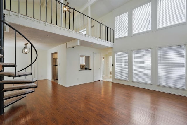 9826 Bent Branch Ln, Dallas, TX 75243 - unfurnished living room featuring a high ceiling, stairs, wood finished floors, baseboards, and plenty of natural light