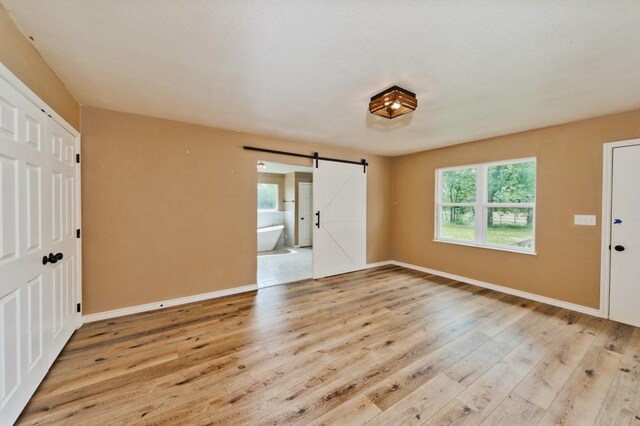 1941 State Highway 59 S, Bowie, TX 76230 - unfurnished bedroom with a barn door, wood finished floors, baseboards, and ensuite bathroom
