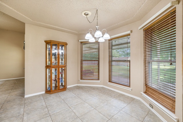unfurnished dining area with light tile patterned floors, a chandelier, a textured ceiling, and baseboards