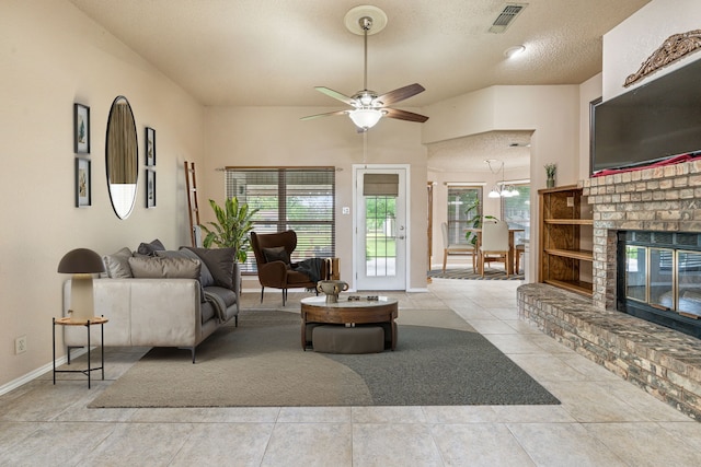 living area featuring a ceiling fan, baseboards, a fireplace, a textured ceiling, and tile patterned floors