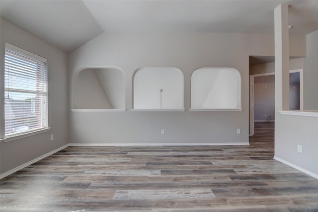 empty room featuring wood finished floors, vaulted ceiling, and baseboards