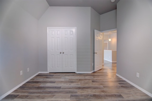 unfurnished bedroom with wood finished floors, baseboards, a closet, and lofted ceiling