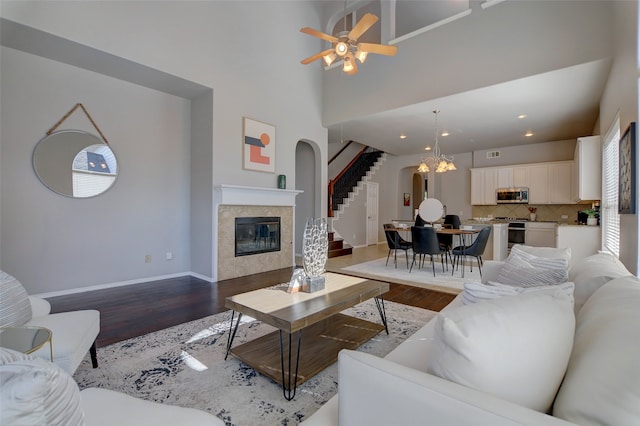 living area with light wood-type flooring, arched walkways, a tiled fireplace, baseboards, and stairway