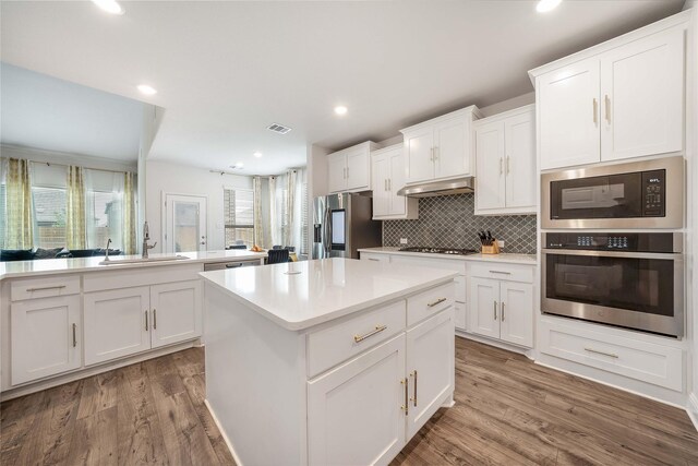 2507 Henley Way, Mansfield, TX 76084 - kitchen with appliances with stainless steel finishes, a sink, under cabinet range hood, a center island, and backsplash