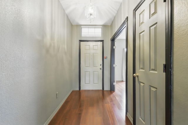 doorway featuring dark wood-style flooring, a chandelier, baseboards, and a textured wall