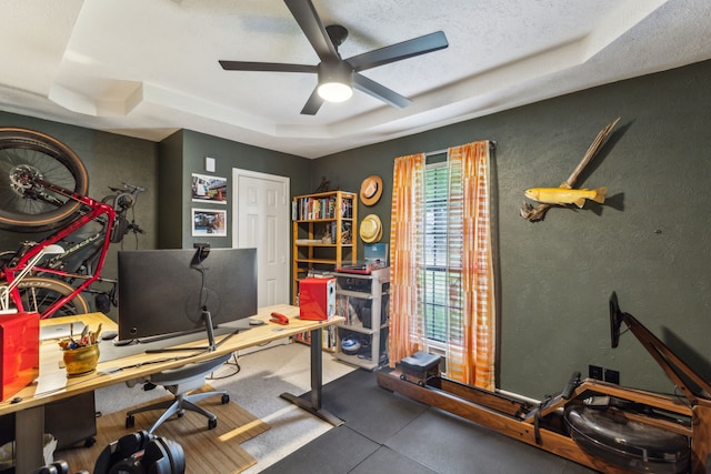 office area featuring a tray ceiling, a ceiling fan, and a textured wall