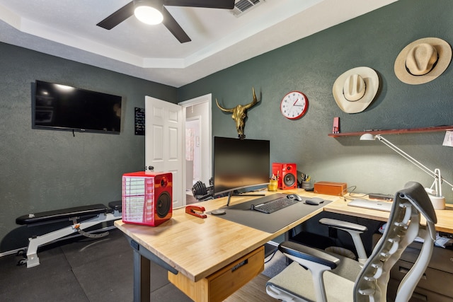 office with a ceiling fan, a textured wall, and a tray ceiling