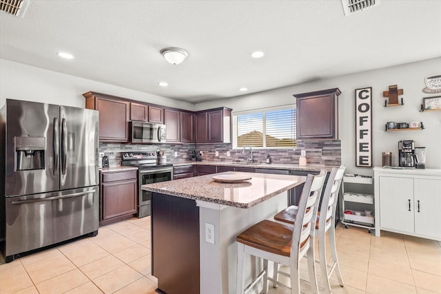 240 Willow Creek Ln, Terrell, TX 75160 - kitchen featuring appliances with stainless steel finishes, light tile patterned floors, decorative backsplash, a kitchen breakfast bar, and light stone countertops