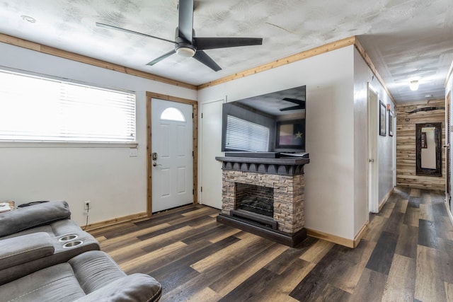 living area featuring ceiling fan, baseboards, wood finished floors, and a stone fireplace