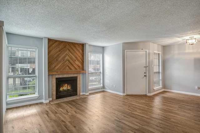 12480 Abrams Rd Unit 2801, Dallas, TX 75243 - unfurnished living room with wood finished floors, healthy amount of natural light, a tiled fireplace, baseboards, and a textured ceiling