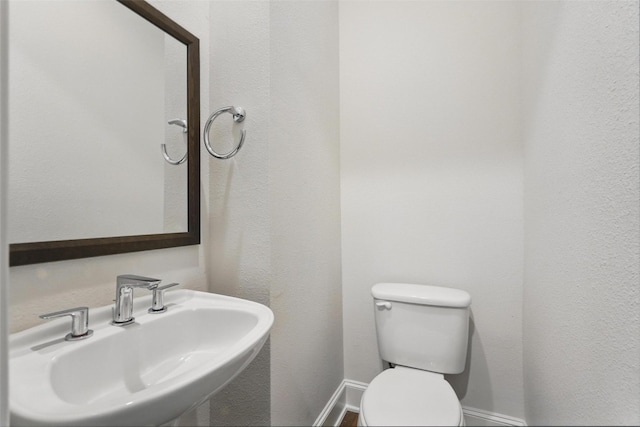 half bathroom featuring a sink, toilet, and baseboards