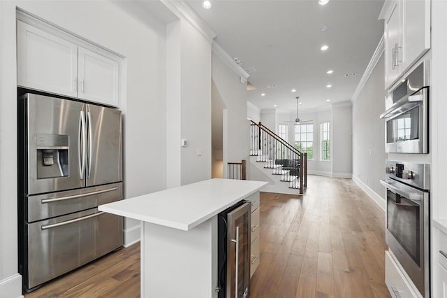 kitchen with stainless steel appliances, ornamental molding, beverage cooler, light wood finished floors, and a kitchen island