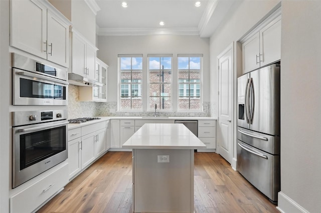 kitchen with stainless steel appliances, a sink, crown molding, a center island, and light countertops