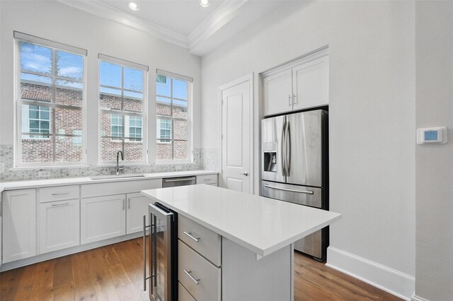 kitchen featuring beverage cooler, stainless steel fridge with ice dispenser, crown molding, a sink, and wood finished floors