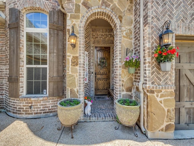 view of exterior entry with brick siding, stone siding, and a porch