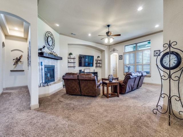 carpeted living room with ornamental molding, arched walkways, ceiling fan, a tile fireplace, and baseboards