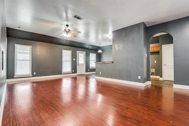 110 Commonwealth Cir, Waxahachie, TX 75165 - unfurnished living room with arched walkways, ceiling fan, wood finished floors, a textured wall, and baseboards