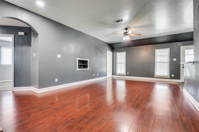 110 Commonwealth Cir, Waxahachie, TX 75165 - unfurnished living room featuring ceiling fan, a textured wall, arched walkways, wood finished floors, and vaulted ceiling