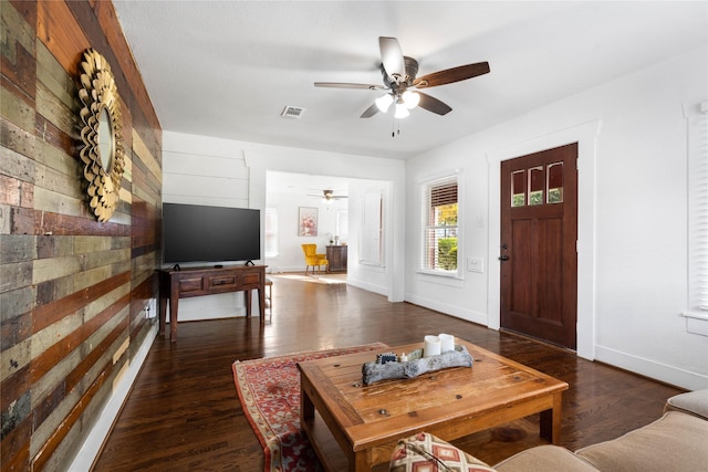 living room with a ceiling fan, baseboards, wooden walls, and wood finished floors