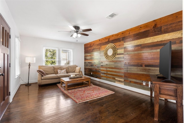 living area with wood walls, ceiling fan, baseboards, and wood finished floors