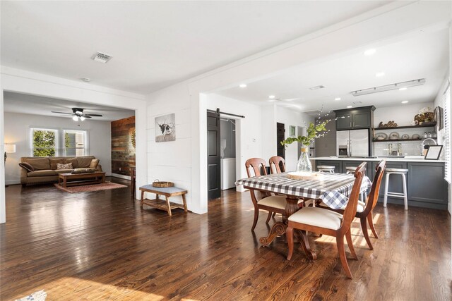 dining room featuring a barn door, dark wood-style floors, and a ceiling fan