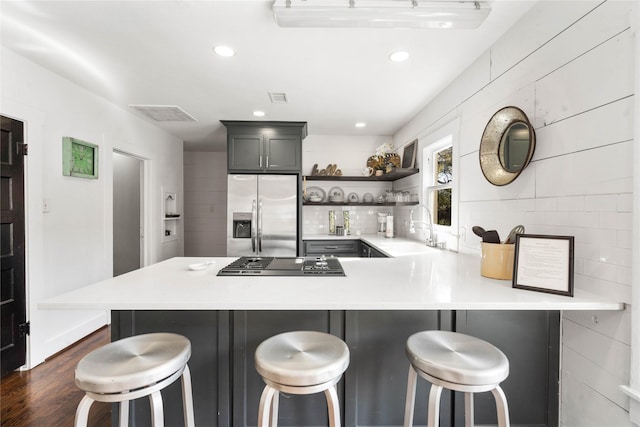 kitchen with stainless steel fridge with ice dispenser, a sink, open shelves, stovetop, and light countertops