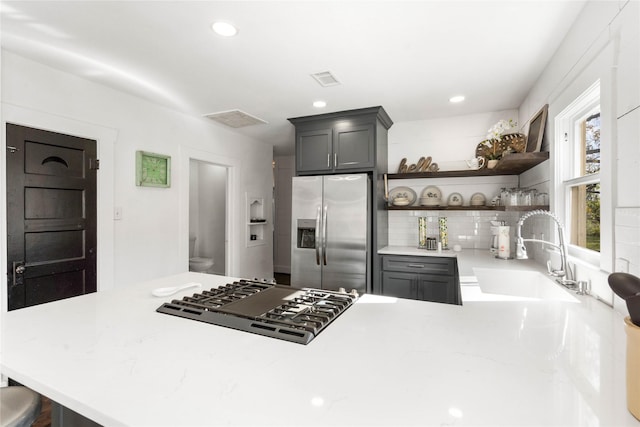 kitchen featuring stainless steel refrigerator with ice dispenser, a sink, gas cooktop, open shelves, and decorative backsplash