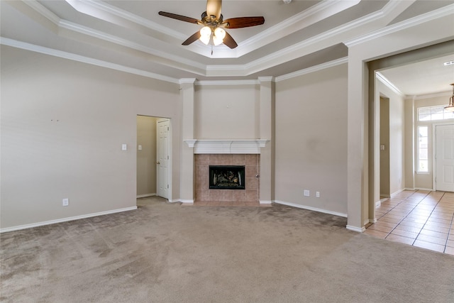 unfurnished living room with crown molding, carpet flooring, a tray ceiling, a ceiling fan, and a tiled fireplace