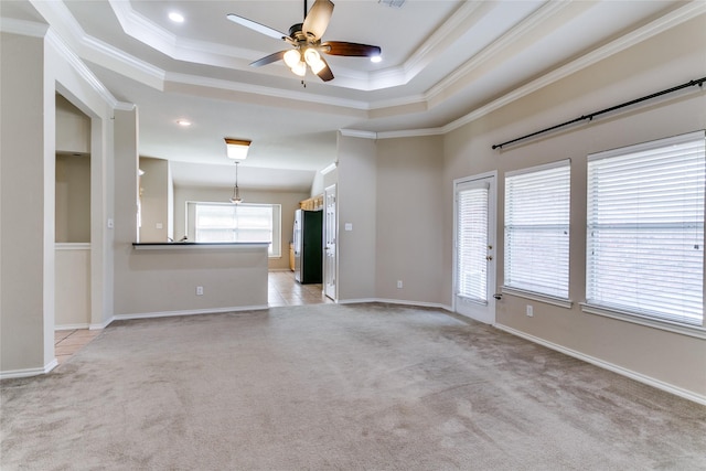 spare room with light carpet, ceiling fan, ornamental molding, a raised ceiling, and baseboards