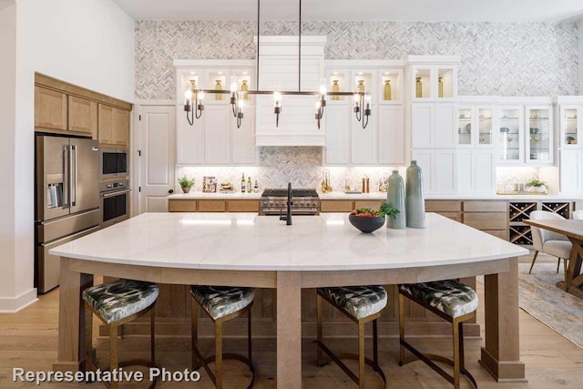 1409 Sire Ct, Aubrey, TX 76227 - kitchen featuring premium appliances, a breakfast bar area, light wood-type flooring, a large island, and decorative backsplash