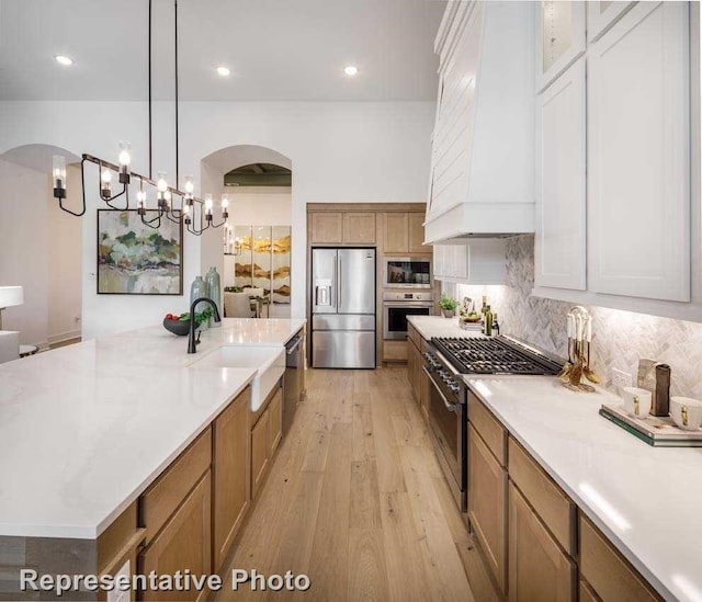 1409 Sire Ct, Aubrey, TX 76227 - kitchen featuring stainless steel appliances, a sink, arched walkways, light wood-style flooring, and backsplash