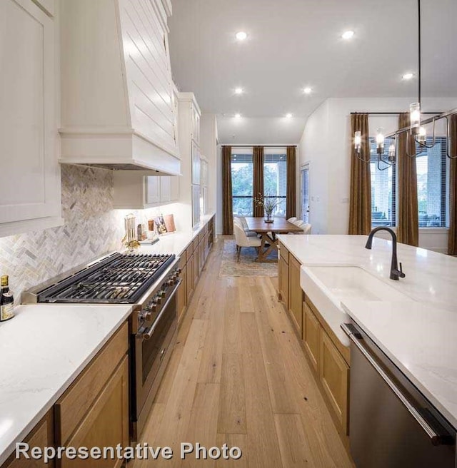 1409 Sire Ct, Aubrey, TX 76227 - kitchen featuring appliances with stainless steel finishes, custom range hood, light wood-type flooring, decorative backsplash, and a chandelier