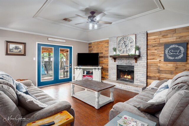 living room featuring wood finished floors, a raised ceiling, a ceiling fan, a brick fireplace, and french doors